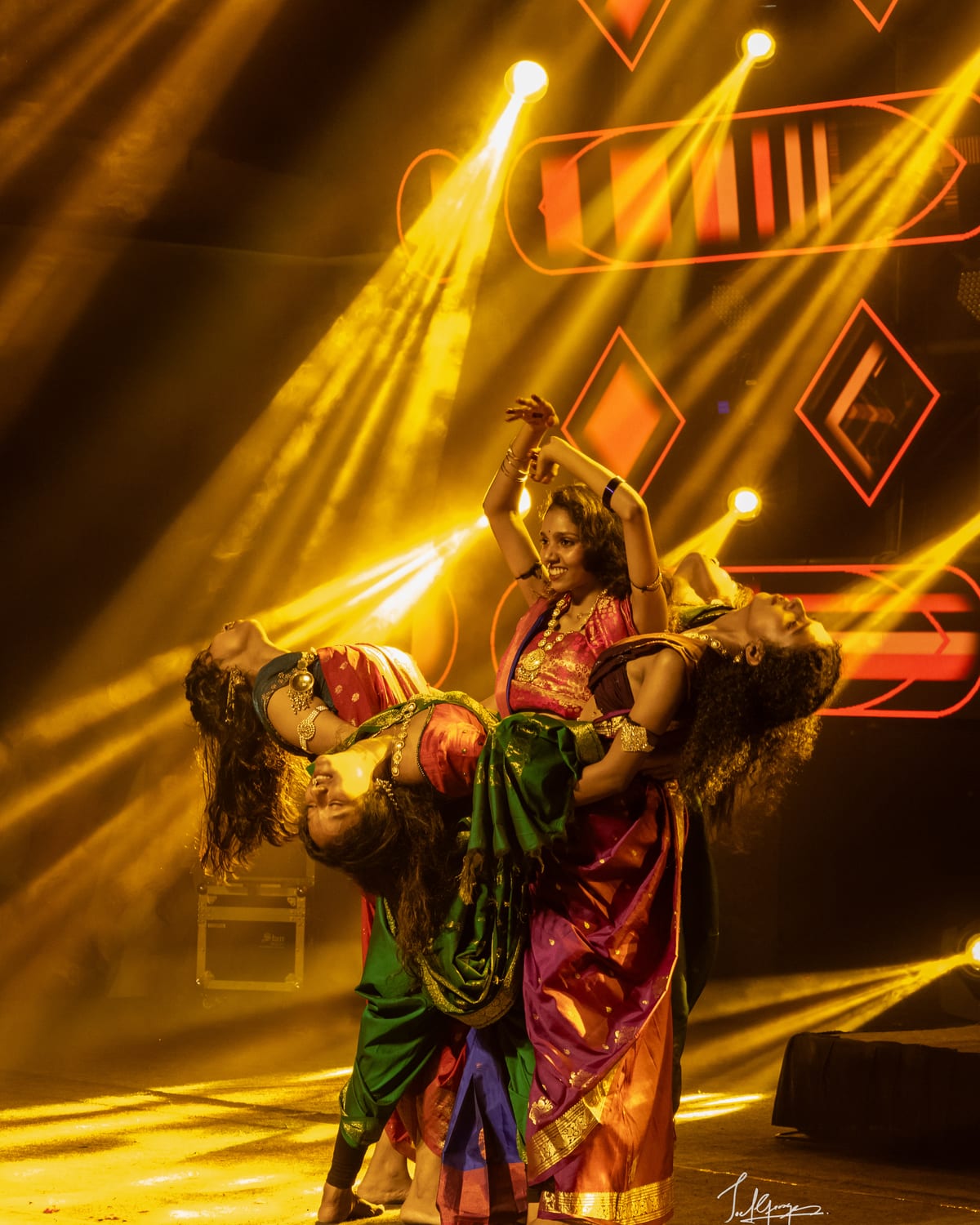 Dancers in saris caught mid-movement under gold stage light