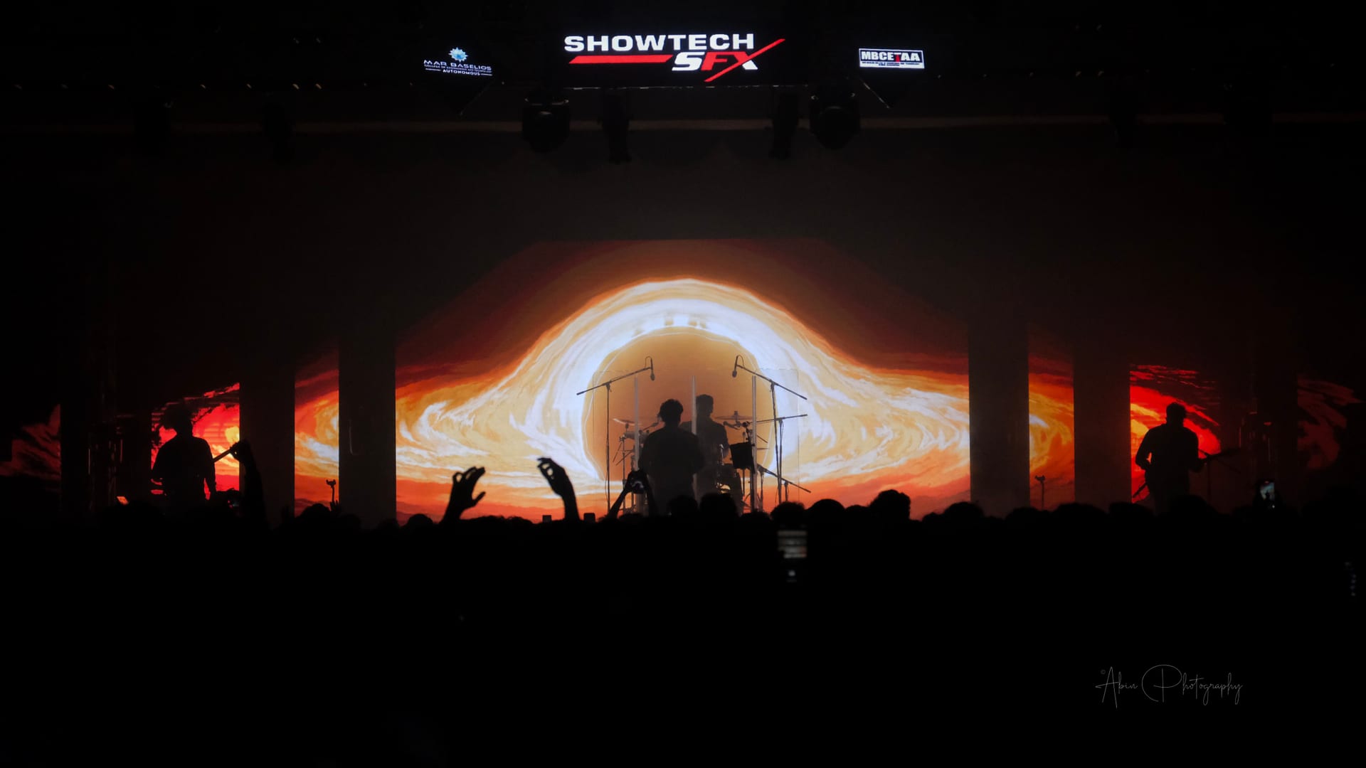 A band silhouetted against a lit backdrop, hands raised in the crowd