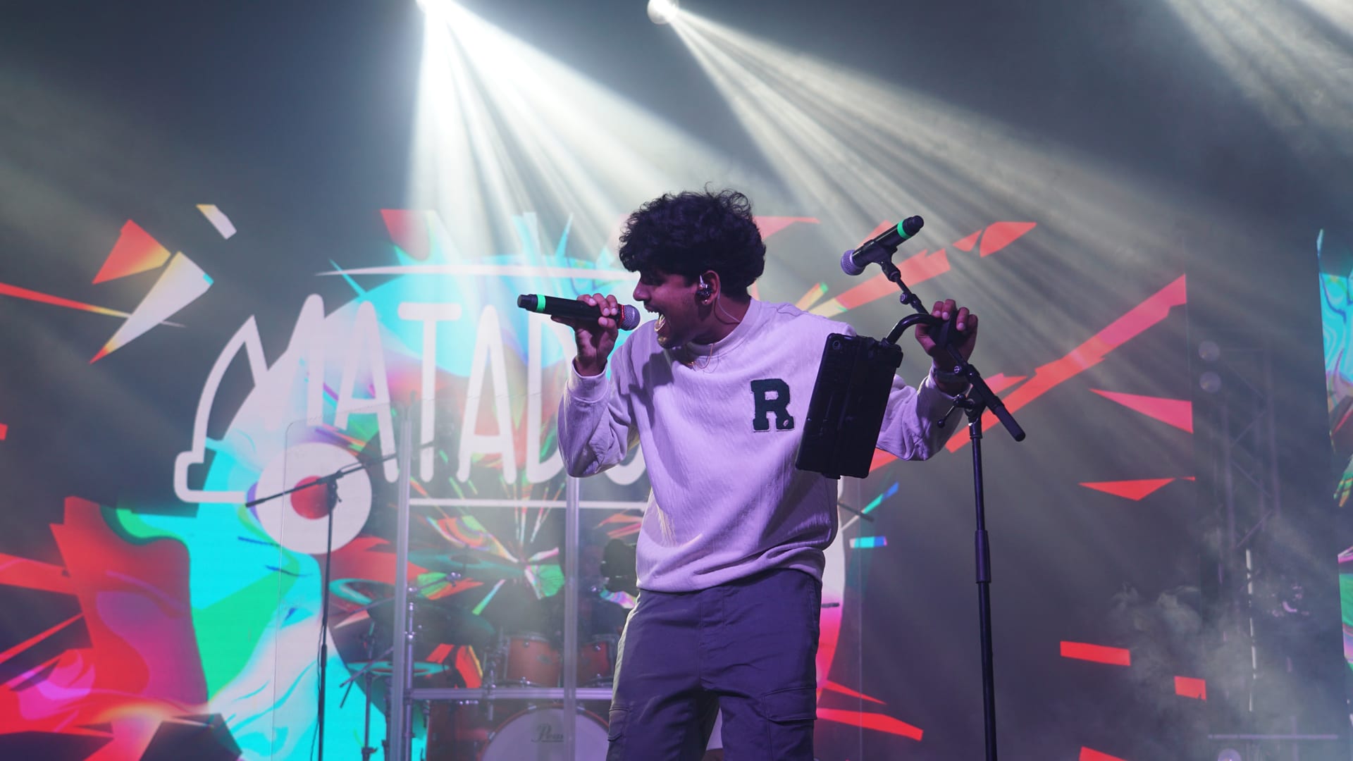 A vocalist mid-line under stage lights, microphone raised